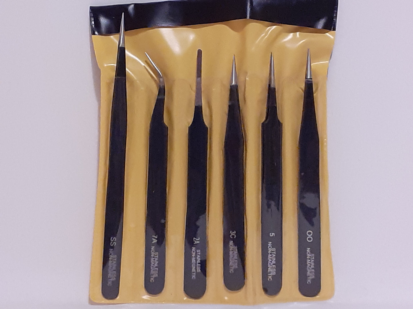 A set of black tweezers in various styles packaged in a clear plastic case with a yellow lining.
